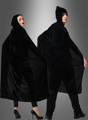 Zwei Personen, die den „Samt Umhang schwarz 140 cm“ tragen – lange, schwarze Samtumhänge mit Kapuze über schwarzer Kleidung –, stehen nebeneinander vor einem grauen Hintergrund mit Farbverlauf – perfekt als geheimnisvolles Halloween-Kostüm.