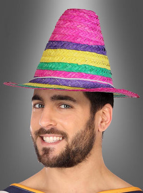 Ein bärtiger Mann lächelt, während er den „Kleiner Mexikaner Hut“-Hut trägt, einen hohen, farbenfrohen, geflochtenen Hut mit Streifen in Rosa, Gelb, Grün und Lila.