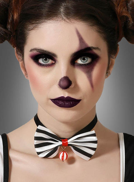 Eine Frau mit Clown-Make-up, dunklem Lidschatten, einer bemalten Nase und einem Stern neben dem Auge, die das schwarz-weiße „Fliege zum Clownskostüm“ trägt, ergänzt durch eine rote Glocke als perfektes Clown-Accessoire.