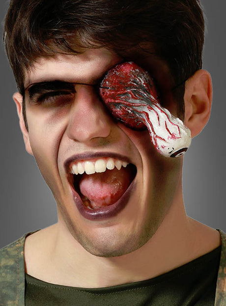 Einem Mann mit offenem Mund ragt ein blutiger, realistisch aussehender künstlicher Augapfel aus der rechten Augenhöhle heraus – ein grausiger Effekt, der mit dem Halloween-Make-up „Heraushängendes Auge“ erzielt wird.