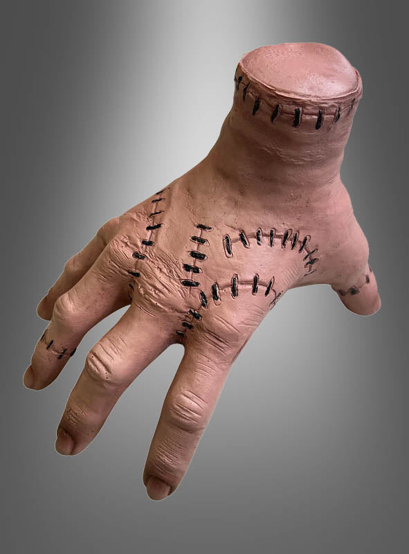 Wir präsentieren die „Halloween-Hand mit Nähten“: eine realistisch gestaltete Requisite in Form einer abgetrennten Hand mit genähten Wunden und ohne Handgelenk, präsentiert vor einem grau verlaufenden Hintergrund.