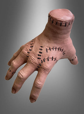 Wir präsentieren die „Halloween-Hand mit Nähten“: eine realistisch gestaltete Requisite in Form einer abgetrennten Hand mit genähten Wunden und ohne Handgelenk, präsentiert vor einem grau verlaufenden Hintergrund.
