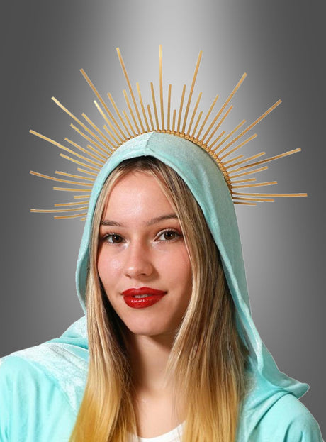 Eine Frau mit langen blonden Haaren, rotem Lippenstift und einer hellblauen Kapuze trägt den goldenen Haarreif „Göttlicher Heiligenschein“ und steht vor einem grauen Hintergrund mit Farbverlauf.