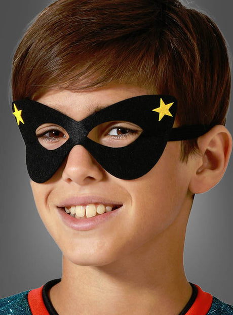 Ein Kind, das eine schwarze Superhelden-Augenmaske für Kinder mit gelben Sternen trägt, lächelt und schaut leicht zur Seite.