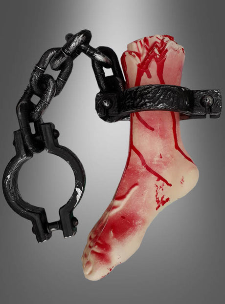 Die Dekoration „Horror – abgetrennter Fuß an einer Kette“ besteht aus einem realistisch gestalteten künstlichen abgetrennten Fuß mit roter Farbe, die Blut imitiert, der an einem großen schwarzen Schäkel und einer Kette befestigt ist und vor einem grauen Hintergrund präsentiert wird – ideal als Halloween-Deko für Ihre nächste Gruselparty.