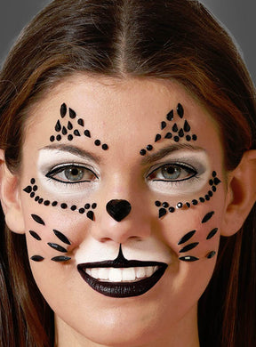 Eine Frau mit einer von Katzen inspirierten Gesichtsbemalung aus schwarz-weißem Make-up, Strasssteinen aus dem Schminkset „Katze mit Edelsteinen“, einer schwarzen Nase und Schnurrhaarmustern lächelt vor einem grauen Hintergrund in die Kamera.