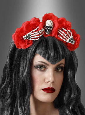 Eine Frau mit dunklem Haar trägt den Halloween-Haarreif mit Blumen und Skelett – ein rotes Blumenstirnband, das mit Skeletthänden und einem Totenkopf verziert ist. Ihr auffälliges Make-up mit dunklem Lidschatten und leuchtend rotem Lippenstift macht dieses Accessoire zum idealen Halloween-Accessoire, um dein „Día de los Muertos“-Kostüm zu vervollständigen – alles vor einem grauen Hintergrund mit Farbverlauf.
