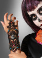 Eine Person mit lila Haaren und „Day of the Dead“-Make-up präsentiert die „Tag der Toten“-Armstulpe aus Spitze – einen schwarzen Spitzenhandschuh, verziert mit bunten Perlen und einem Totenkopf-Anhänger – und streckt ihre Hand vor einem grauen Hintergrund in die Höhe; dieses elegante Accessoire mit aufwendigen Spitzendetails eignet sich perfekt für jedes „Día de los Muertos“-Kostüm.
