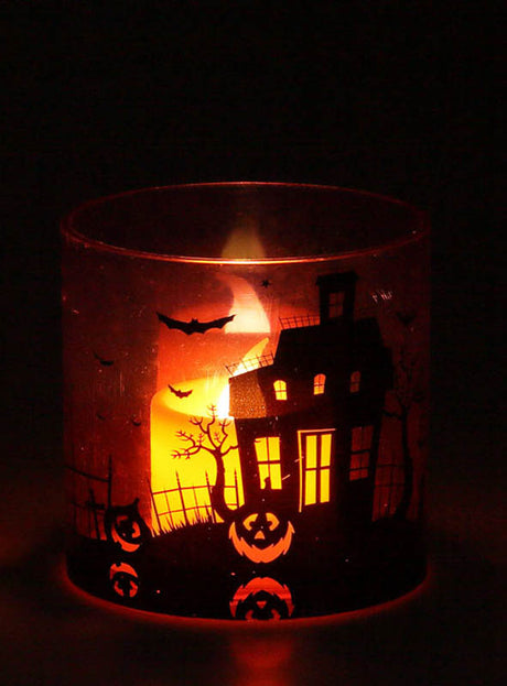 Ein leuchtendes Windlicht „Halloween mit Licht“ (7 cm) strahlt aus seinem Halter heraus in die Dunkelheit. Der Halter ist mit Halloween-Motiven wie einem Spukhaus, Fledermäusen, Bäumen und Kürbislaternen verziert. Dieses bezaubernde Licht ist die perfekte Halloween-Dekoration, um eine gruselige und zugleich einladende Atmosphäre zu schaffen.