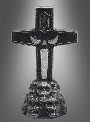 Der „Leuchtender Grabstein LED 11 cm“ zeigt ein schwarzes Kreuz mit einem Fledermaus-Symbol, das auf einem Sockel aus reliefartig gestalteten Totenköpfen vor einem grauen Hintergrund mit Farbverlauf steht.