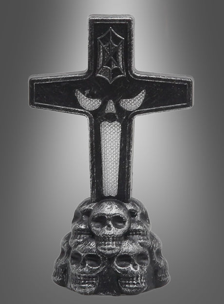 Der „Leuchtender Grabstein LED 11 cm“ zeigt ein schwarzes Kreuz mit einem Fledermaus-Symbol, das auf einem Sockel aus reliefartig gestalteten Totenköpfen vor einem grauen Hintergrund mit Farbverlauf steht.