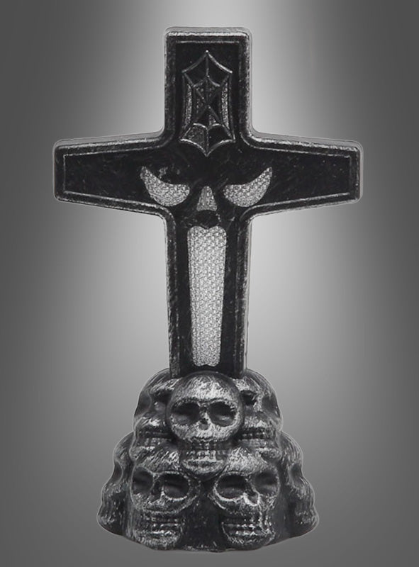 Der „Leuchtender Grabstein LED 11 cm“ zeigt ein schwarzes Kreuz mit einem Fledermaus-Symbol, das auf einem Sockel aus reliefartig gestalteten Totenköpfen vor einem grauen Hintergrund mit Farbverlauf steht.