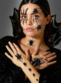 Eine Frau mit nach hinten geglätteten Haaren trägt ein schwarzes Outfit und hat ein von den „Großen Spinnen-Tattoos“ zu Halloween inspiriertes Spinnen-Make-up im Gesicht und an den Händen, mit aufgemalten Spinnen und Spinnennetzen vor grauem Hintergrund.