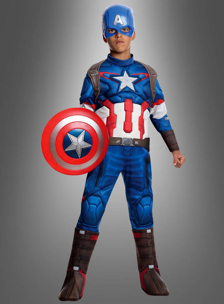 Ein Kind steht vor einem schlichten grauen Hintergrund, trägt ein klassisches blau-rot-weißes Captain-America-Kostüm mit Maske und hält das Captain-America-Schutzschild (klein, 30 cm) in der Hand.