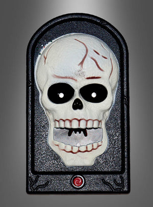 Die „Türklingel Skelett Totenschädel Halloween“ ist in einen schwarzen, gewölbten Rahmen mit einem roten Knopf an der Unterseite eingefasst und verfügt über einen Kunststoffschädel mit markanten schwarzen Augenhöhlen und leuchtend roten Rissen – damit ist sie ein auffälliges Halloween-Dekostück mit Totenschädel-Motiv oder ein Akzent im Horror-Stil für Ihren Eingangsbereich, hier abgebildet vor einem grauen Hintergrund mit Farbverlauf.