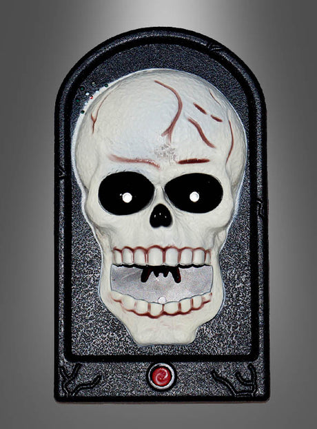 Die „Türklingel Skelett Totenschädel Halloween“ ist in einen schwarzen, gewölbten Rahmen mit einem roten Knopf an der Unterseite eingefasst und verfügt über einen Kunststoffschädel mit markanten schwarzen Augenhöhlen und leuchtend roten Rissen – damit ist sie ein auffälliges Halloween-Dekostück mit Totenschädel-Motiv oder ein Akzent im Horror-Stil für Ihren Eingangsbereich, hier abgebildet vor einem grauen Hintergrund mit Farbverlauf.