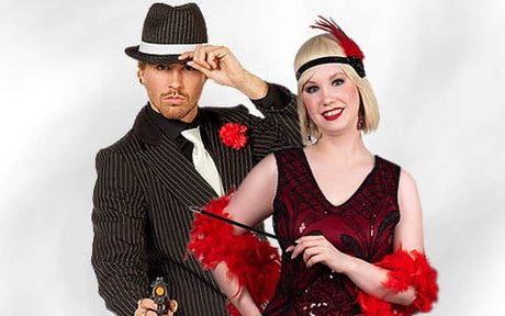 Ein Mann in einem Nadelstreifenanzug und einem Fedora posiert mit einer Spielzeugpistole neben einer lächelnden Frau in einem Flapper-Kleid mit Feder-Accessoires.