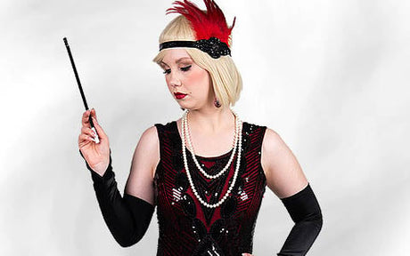 Frau in der Flapper-Mode der 1920er Jahre mit einem roten Stirnband mit Federn, langen Perlenketten, schwarzen Handschuhen und einer Zigarettenspitze in der Hand.