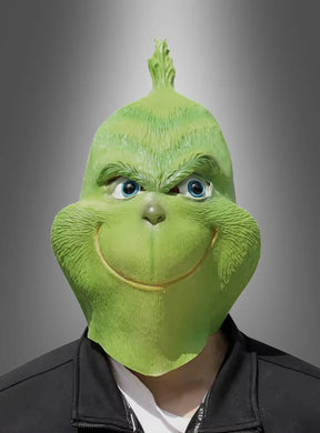 Eine Person, die die grüne Monster-Vollmaske aus Latex trägt, steht vor einem grauen Hintergrund mit Farbverlauf und ist mit einer schwarzen Jacke bekleidet. Dieses auffällige Weihnachtskostüm verleiht der Szene eine verspielte, schelmische Note.