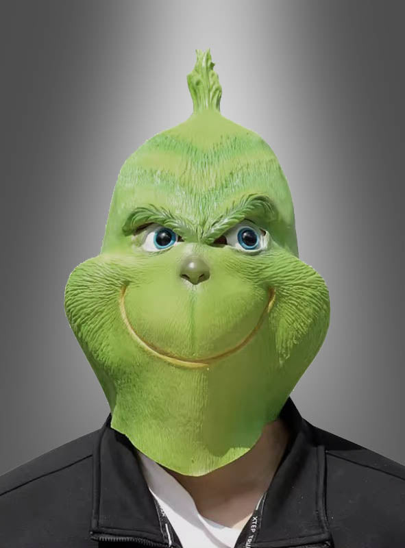 Eine Person, die die grüne Monster-Vollmaske aus Latex trägt, steht vor einem grauen Hintergrund mit Farbverlauf und ist mit einer schwarzen Jacke bekleidet. Dieses auffällige Weihnachtskostüm verleiht der Szene eine verspielte, schelmische Note.