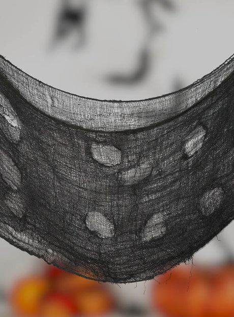 Eine Nahaufnahme des „Riesiges Stofftuch 172x76cm Halloween grau“ – ein transparenter grauer Stoff mit einem gruseligen Muster –, der vor einem unscharfen Hintergrund mit orangefarbenen Formen drapiert ist und sich perfekt als gruseliger Dekostoff eignet.
