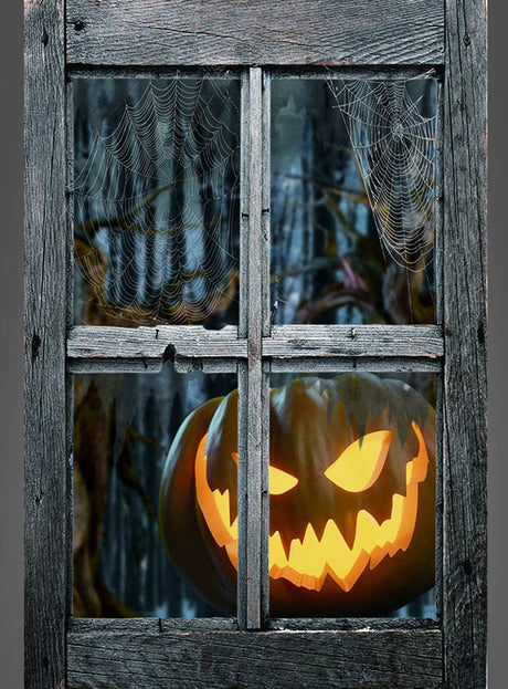 Durch ein altes, mit Spinnweben behangenes Holzfenster scheint eine leuchtende Kürbislaterne mit einem unheimlichen Kürbisgesicht – die Halloween-Kürbis-Fensterdekoration (80 x 120 cm) präsentiert sich damit als ideale Dekoration vor einer gruseligen Waldkulisse.