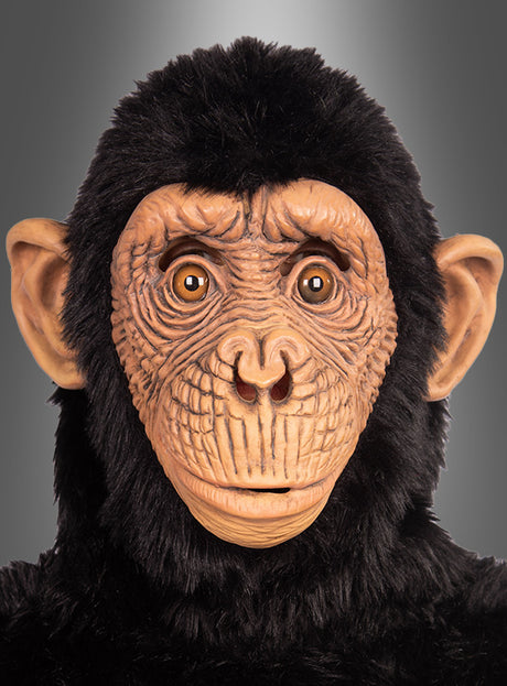 Vor einem neutralen grauen Hintergrund ist eine Person zu sehen, die die „Realistische Affenmaske für Erwachsene“ mit detaillierten Gesichtszügen und schwarzem Fell trägt. Diese hochwertige Latex-Affenmaske für Erwachsene fängt das lebensechte Wesen eines Schimpansen ein.