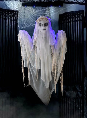 Die 120 cm große „Schwebende Geisterbraut“ ist eine beeindruckende Halloween-Dekoration: Sie hängt vor schwarzen Toren, trägt weiße, zerfetzte Gewänder sowie eine kronenähnliche Kopfbedeckung und hat hohle Augen, die von blauen Lichtern beleuchtet werden.