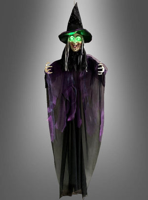Eine Halloween-Dekoration mit der „Sprechenden Hexe“ (183 cm) mit LED-Augen: Diese Hexe steht vor einem grauen Hintergrund und hat leuchtend grüne LED-Augen, einen schwarzen Spitzhut und eine lange schwarz-lila Robe.
