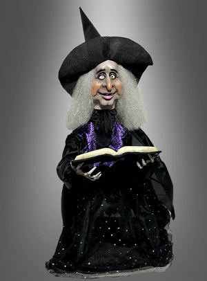 Die „Animierte Hexe mit Zauberbuch 70 cm Halloween“ zeigt eine Hexenpuppe mit spitzem Hut und grauen Haaren, die ein aufgeschlagenes Zauberbuch in der Hand hält. Sie trägt eine schwarz-lila Robe und steht vor einem grauen Hintergrund mit Farbverlauf – perfekt als Hexendekoration oder Halloween-Deko, um Ihren Feierlichkeiten einen gruseligen Touch zu verleihen.