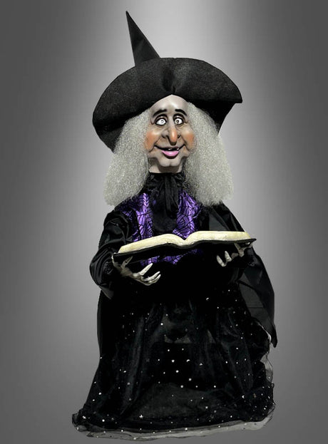 Die „Animierte Hexe mit Zauberbuch 70 cm Halloween“ zeigt eine Hexenpuppe mit spitzem Hut und grauen Haaren, die ein aufgeschlagenes Zauberbuch in der Hand hält. Sie trägt eine schwarz-lila Robe und steht vor einem grauen Hintergrund mit Farbverlauf – perfekt als Hexendekoration oder Halloween-Deko, um Ihren Feierlichkeiten einen gruseligen Touch zu verleihen.