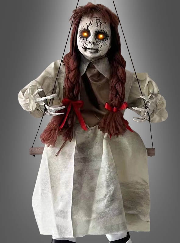 Schaukelnde Zombie-Puppe, 80 cm groß, mit leuchtend orangefarbenen Augen, zerfurchtem Gesicht, geflochtenen roten Haaren und weißem Kleid – perfekt als gruselige Halloween-Dekoration vor grauem Hintergrund.