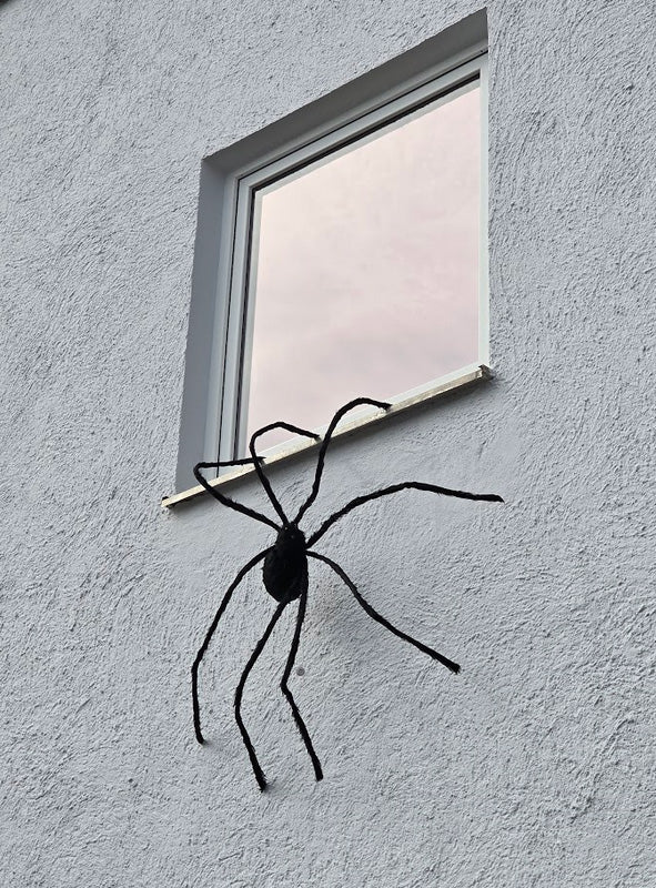 An der Außenwand unterhalb eines Fensters eines grauen Gebäudes ist eine schwarze Riesenspinne (150 cm) mit LED-Augen angebracht, die eine auffällige Halloween-Spinnendekoration bildet.