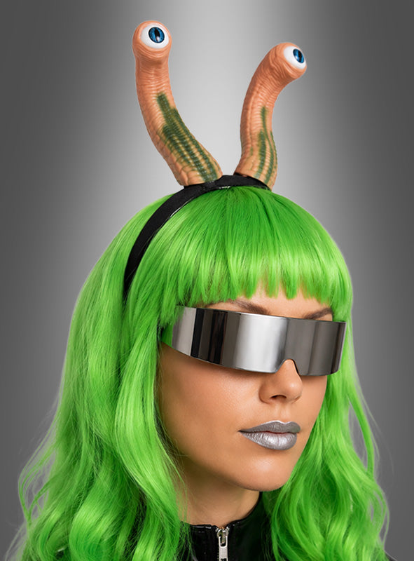 Eine Person mit grüner Perücke, silbernem Lippenstift, übergroßer silberner Sonnenbrille und dem „Alien Haarreif mit Augen“ – komplett mit zwei Stielaugen, die an die Augenstiele einer Schnecke erinnern – posiert vor einem grauen Hintergrund mit Farbverlauf und bildet damit das perfekte Outfit für eine Veranstaltung zum Thema Weltraum.