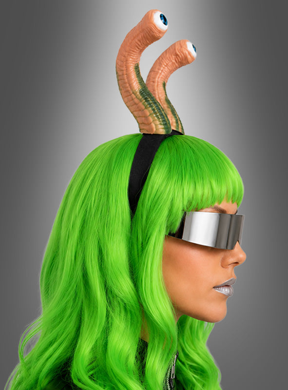 Eine Person mit einer leuchtend grünen Perücke, einer metallischen Sonnenbrille und einem Stirnband mit dem „Alien Haarreif mit Augen“ vor einem grauen Hintergrund mit Farbverlauf – die perfekte Kleidung für jedes ausgefallene Weltraum-Event.