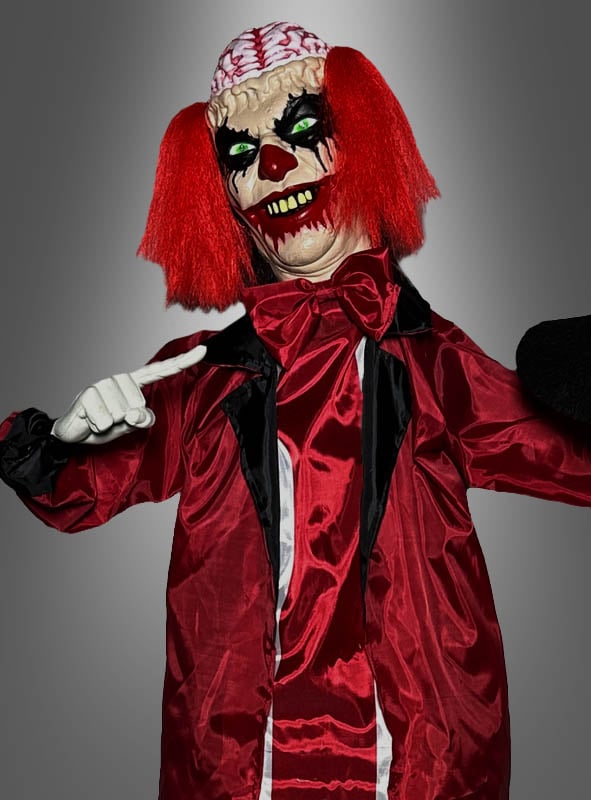 Eine Person, verkleidet als „Animierter Zombie-Clown 170 cm“ – ein animatronisches Horror-Clown-Kostüm mit roten Haaren, weißen Handschuhen, einem rot-schwarzen Outfit und einem Design, das ein freiliegendes Gehirn auf dem Kopf zeigt –, steht vor einem grauen Hintergrund.