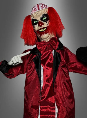 Eine Person, verkleidet als „Animierter Zombie-Clown 170 cm“ – ein animatronisches Horror-Clown-Kostüm mit roten Haaren, weißen Handschuhen, einem rot-schwarzen Outfit und einem Design, das ein freiliegendes Gehirn auf dem Kopf zeigt –, steht vor einem grauen Hintergrund.