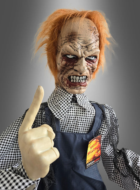 Eine furchteinflößende Halloween-Dekoration, der „Zombie-Totengräber mit Schaufel 160 cm, animiert“, zeigt einen animatronischen Zombie-Totengräber mit zerzaustem orangefarbenem Haar, einem vernarbten Gesicht und einem erhobenen Zeigefinger, der ein kariertes Hemd und eine Schürze trägt und ein „Happy Halloween“-Anstecker.