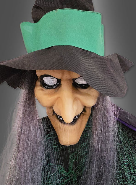 Eine „Fliegende Hexe mit Besen 210 cm Deko“ mit grünem Hutband, langen grauen Haaren, spitzer Nase, schwarzem Mund und einem grünen Netzkleid schwebt vor einem grauen Hintergrund – perfekt als Halloween-Dekoration oder für Fans des klassischen „Hexe mit Besen“-Motivs.