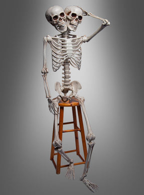 Ein lebensgroßes Menschenskelett (153 cm) mit zwei Köpfen sitzt auf einem Holzstuhl vor grauem Hintergrund – die perfekte Halloween-Dekoration für außergewöhnliche Gruselmomente.
