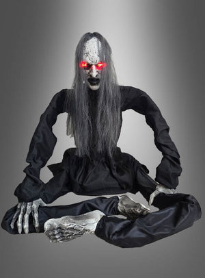 Eine lebensechte Halloween-Requisite in Skelettform mit langen grauen Haaren, leuchtend roten Augen, einem schwarzen Kleid und langgestreckten Gliedmaßen, die mit gekreuzten Beinen vor einem grauen Hintergrund mit Farbverlauf sitzt – diese „Zombie-Figur 60 cm animiert“ wird Ihnen garantiert einen Schauer über den Rücken jagen.