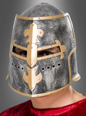 Eine Person, die den „Ritterturnier-Helm mit Visier“ mit goldenen Verzierungen trägt und dazu ein rotes Samtgewand, sichtbar von den Schultern aufwärts vor einem grauen Hintergrund – perfekt für jede Mittelalter- oder Ritterkostüm-Veranstaltung.
