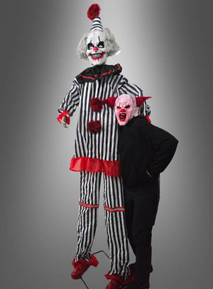 Eine Person in schwarzer Kleidung und einer roten Monstermaske steht neben dem „Hochfahrender Horror Clown 260–300 cm“ (Animatronik) – einer großen Figur mit roten Akzenten, die perfekt die Atmosphäre eines Horror-Clowns für Ihre Halloween-Dekoration vermittelt, vor einem grauen Hintergrund.