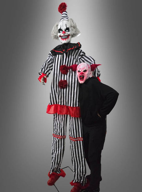 Eine Person in schwarzer Kleidung und einer roten Monstermaske steht neben dem „Hochfahrender Horror Clown 260–300 cm“ (Animatronik) – einer großen Figur mit roten Akzenten, die perfekt die Atmosphäre eines Horror-Clowns für Ihre Halloween-Dekoration vermittelt, vor einem grauen Hintergrund.