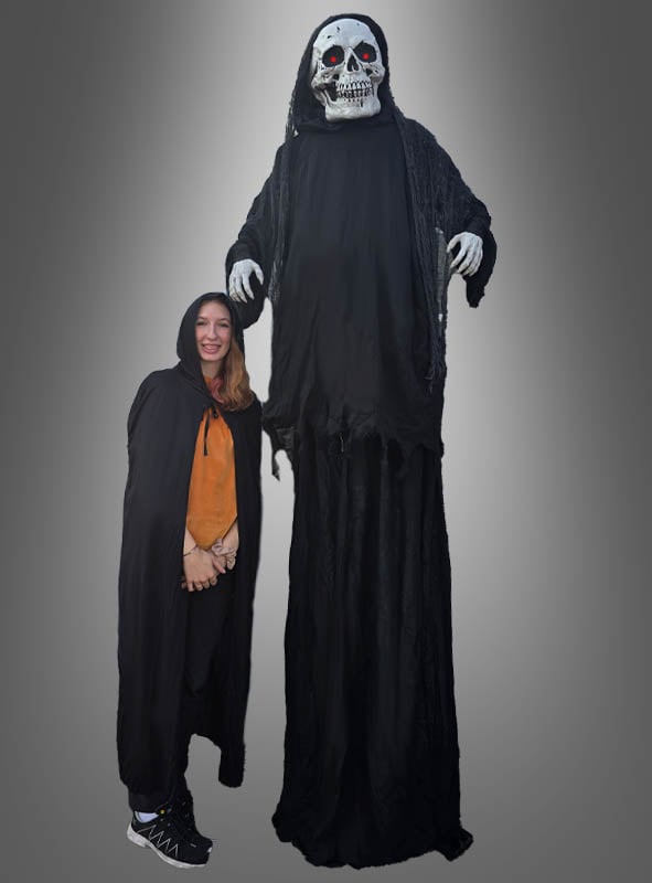 Eine Frau in einem schwarzen Umhang steht neben dem „Riesiger animierter Reaper 265 cm“, einer hoch aufragenden Figur in einem Sensenmann-Kostüm mit Skelettmaske; beide sind vor einem schlichten grauen Hintergrund zu sehen.