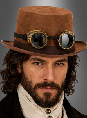 Ein Mann mit einem braunen Zylinderhut im Wildleder-Look und einer Vintage-Schutzbrille, kombiniert mit einem Hemd mit hohem Kragen und einer dunklen Jacke, blickt direkt in die Kamera – ein beeindruckendes Steampunk-Kostüm-Ensemble.
