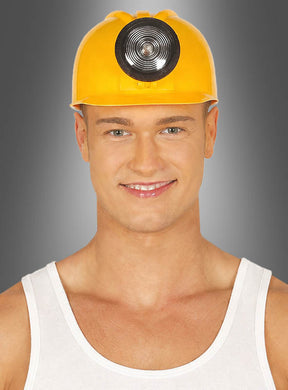 Ein Mann, der einen gelben Bauarbeiterhelm mit Licht trägt – einen klassischen Bauarbeiterhelm, wie man ihn oft in Karnevalskostümen sieht – und ein weißes Tanktop, lächelt vor einem grau verlaufenden Hintergrund in die Kamera.