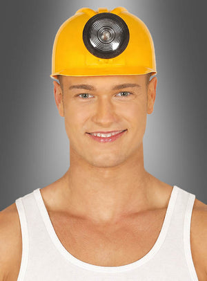 Ein Mann, der einen gelben Bauarbeiterhelm mit Licht trägt – einen klassischen Bauarbeiterhelm, wie man ihn oft in Karnevalskostümen sieht – und ein weißes Tanktop, lächelt vor einem grau verlaufenden Hintergrund in die Kamera.