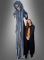 Eine Frau in einem schwarzen Umhang steht neben der „Animierten Halloween-Skelett-Dekoration 255 cm“ – einem imposanten Sensenmann mit Kapuze, Skelettgesicht und zerfetzten Gewändern, der sich perfekt als Halloween-Dekoration eignet – vor einem schlichten grauen Hintergrund.