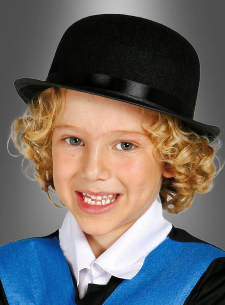 Ein lächelndes Kind mit lockigem blondem Haar, das einen „Schwarze Melone Hut für Kinder“, ein weißes Hemd mit Kragen und eine blaue Weste trägt, vor grauem Hintergrund – perfekt für ein Kostüm im Stil der 20er Jahre.